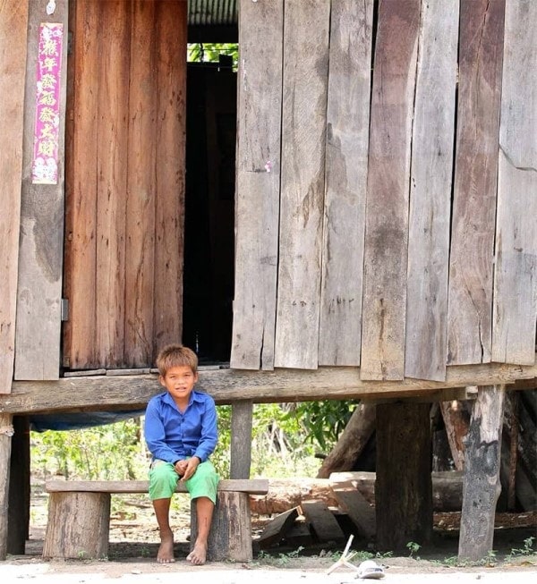 Photo of a young Cambodian boy sitting in front of a traditional family house in the rural countryside featured in Roche Diagram magazine healthcare publications